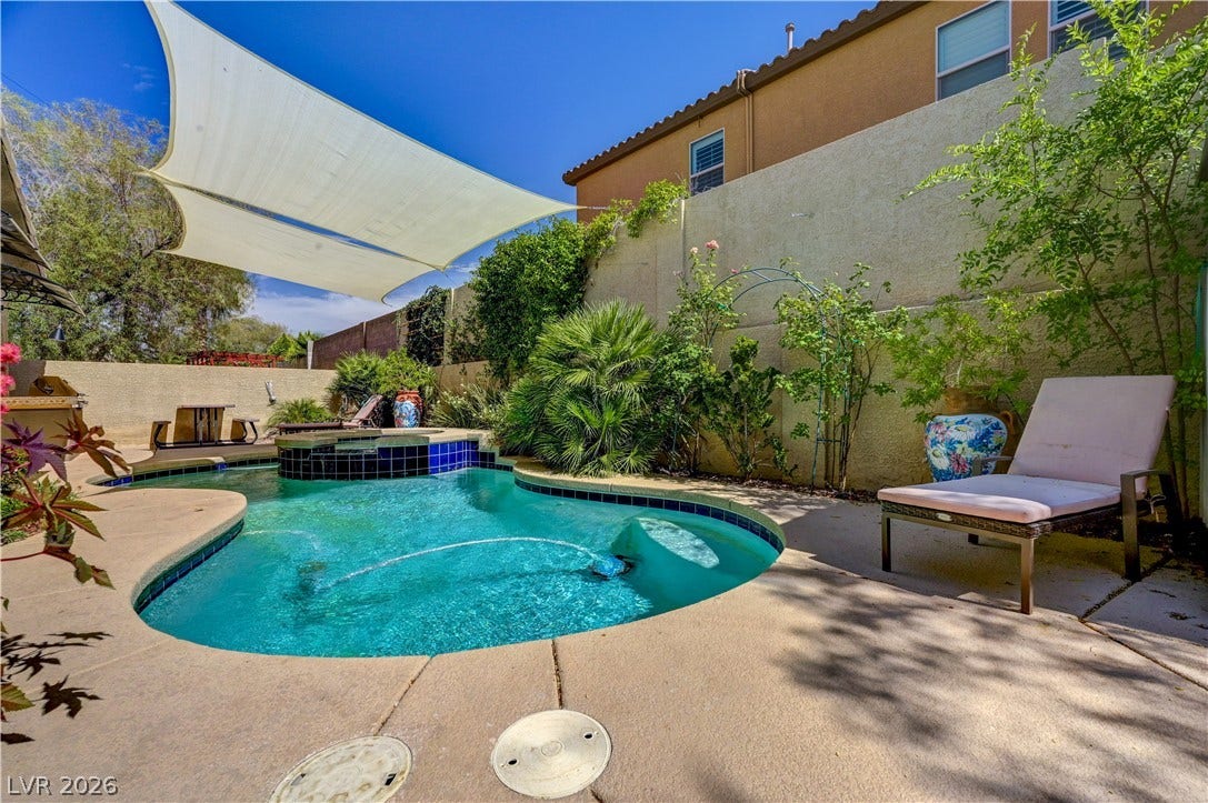 115 Cora Hills Court, Las Vegas, NV 89148 A private backyard oasis features a shimmering pool, surrounded by mature landscaping and a stylish shade sail.