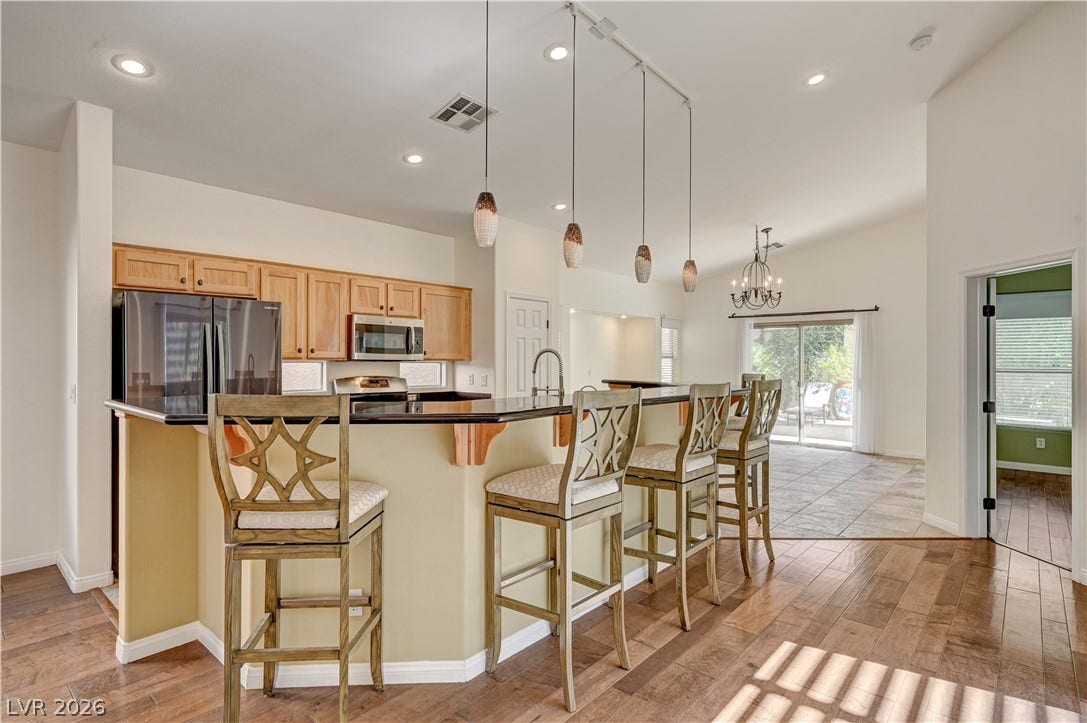 115 Cora Hills Court, Las Vegas, NV 89148 A well-lit kitchen with rich wood flooring and a breakfast bar, seamlessly connected to an outdoor area.