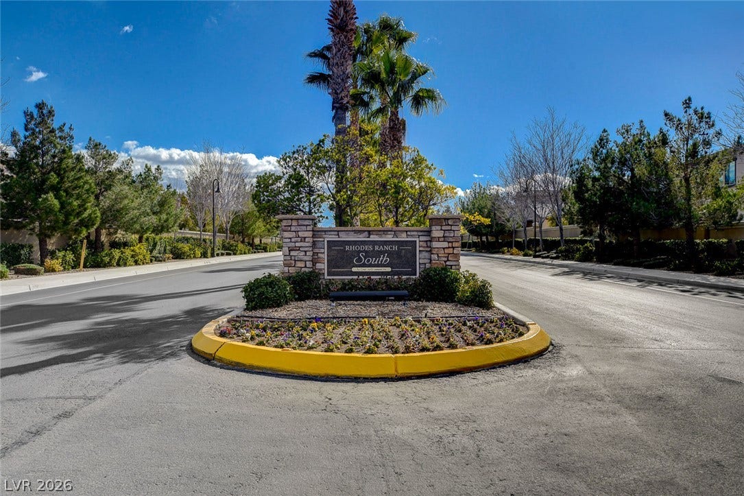 115 Cora Hills Court, Las Vegas, NV 89148 A well-maintained community entrance features stone and brick signage, flanked by verdant landscaping and mature palm trees.
