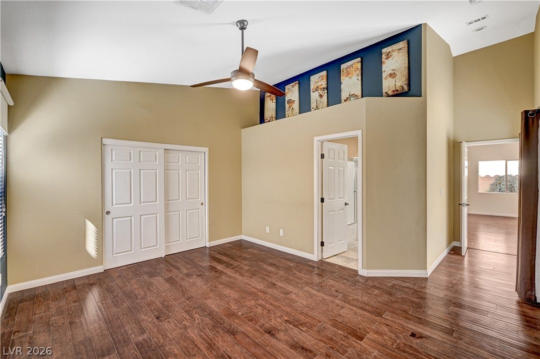 115 Cora Hills Court, Las Vegas, NV 89148 Rich hardwood flooring creates a welcoming ambiance in this spacious sleeping area, featuring convenient closet access and a ceiling fan.