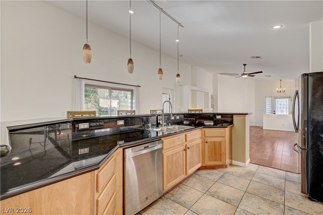 115 Cora Hills Court, Las Vegas, NV 89148 A well-appointed kitchen features dark granite counters, a stainless steel dishwasher, and natural wood cabinetry.