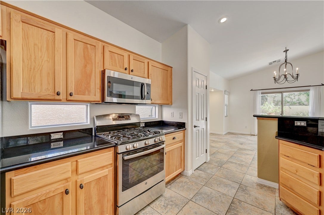 115 Cora Hills Court, Las Vegas, NV 89148 A functional kitchen features sleek granite counters and stainless steel appliances, seamlessly connecting to an airy dining area.