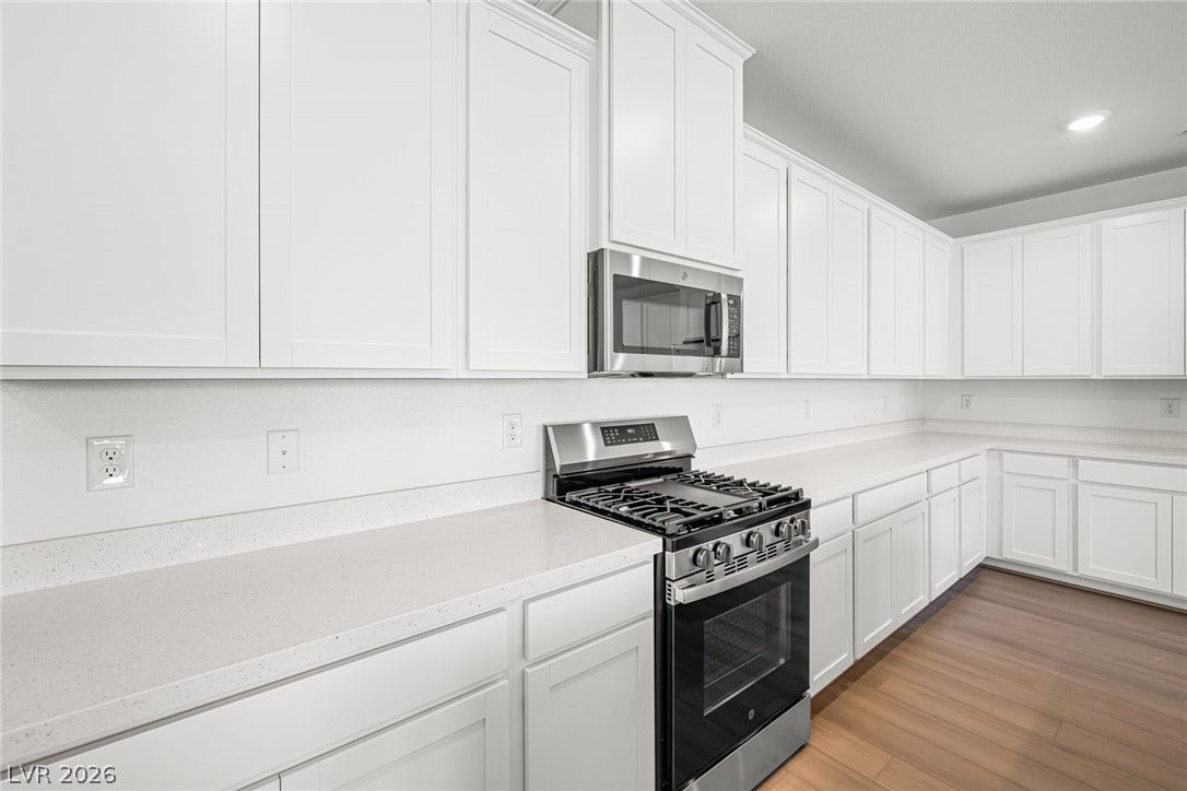 White cabinetry, solid surface counters, and stainless appliances create a pristine kitchen space.