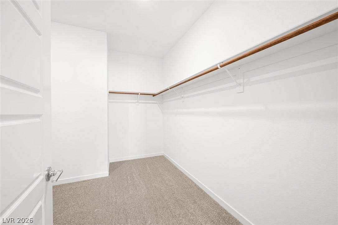 A well-organized walk-in closet with ample hanging space and neutral carpeting.