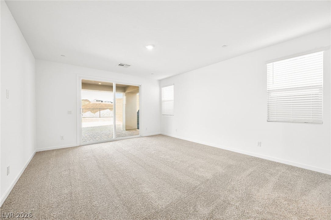 A spacious room offers comfortable carpeting and a sliding glass door to outdoor living.