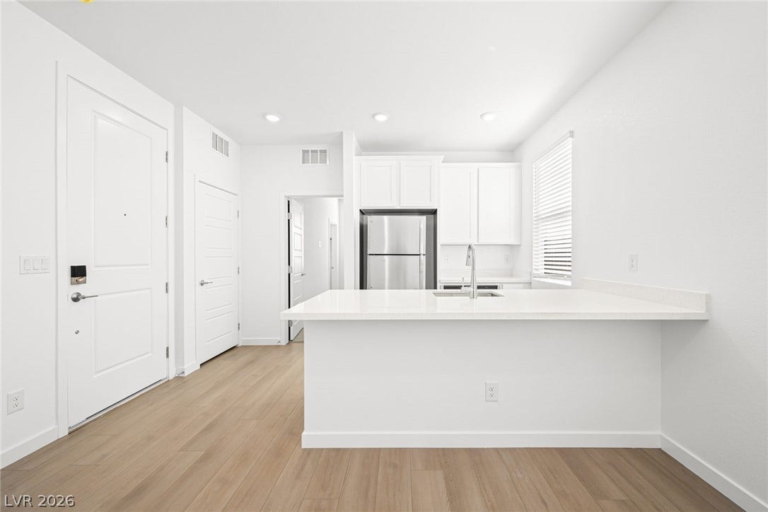 A streamlined kitchen and entry, featuring light wood-look flooring and crisp white cabinetry.