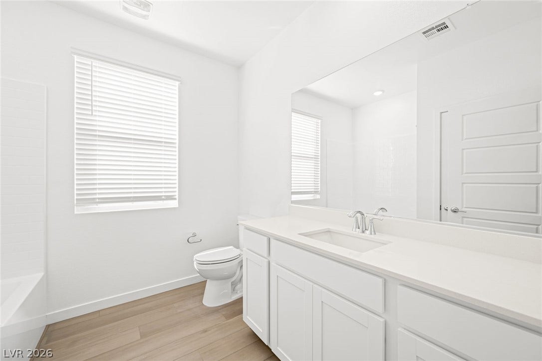 A well-lit bathroom features light wood-look flooring and a white vanity with ample counter space.