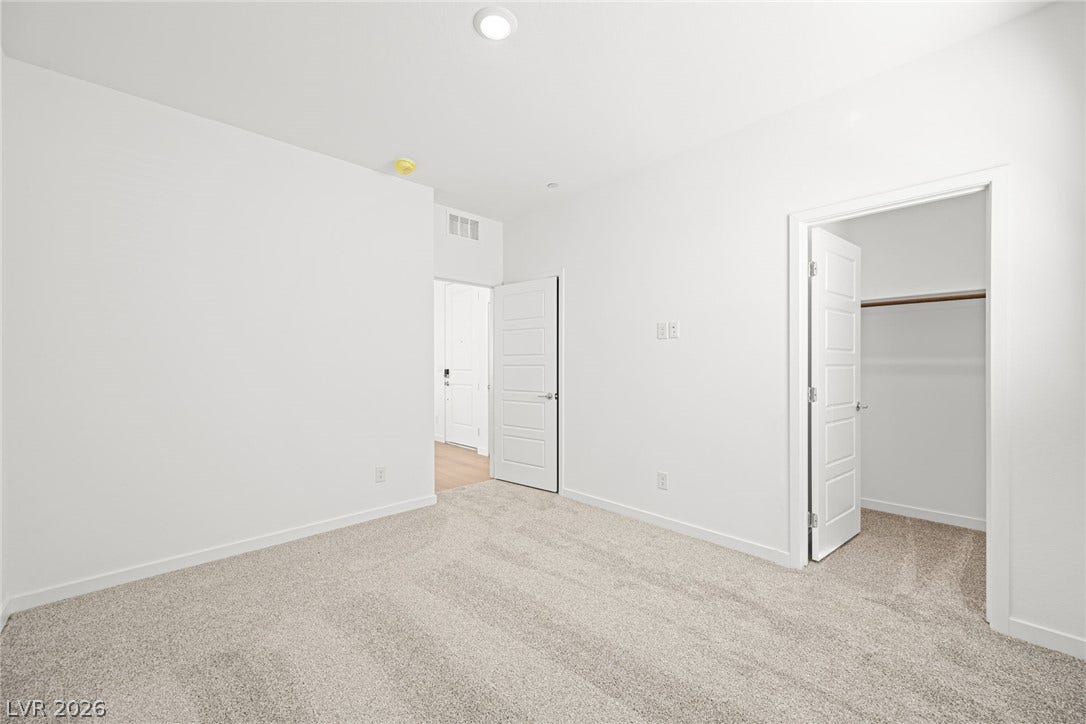 A spacious and neutral bedroom featuring soft carpeting, ideal for personalization.