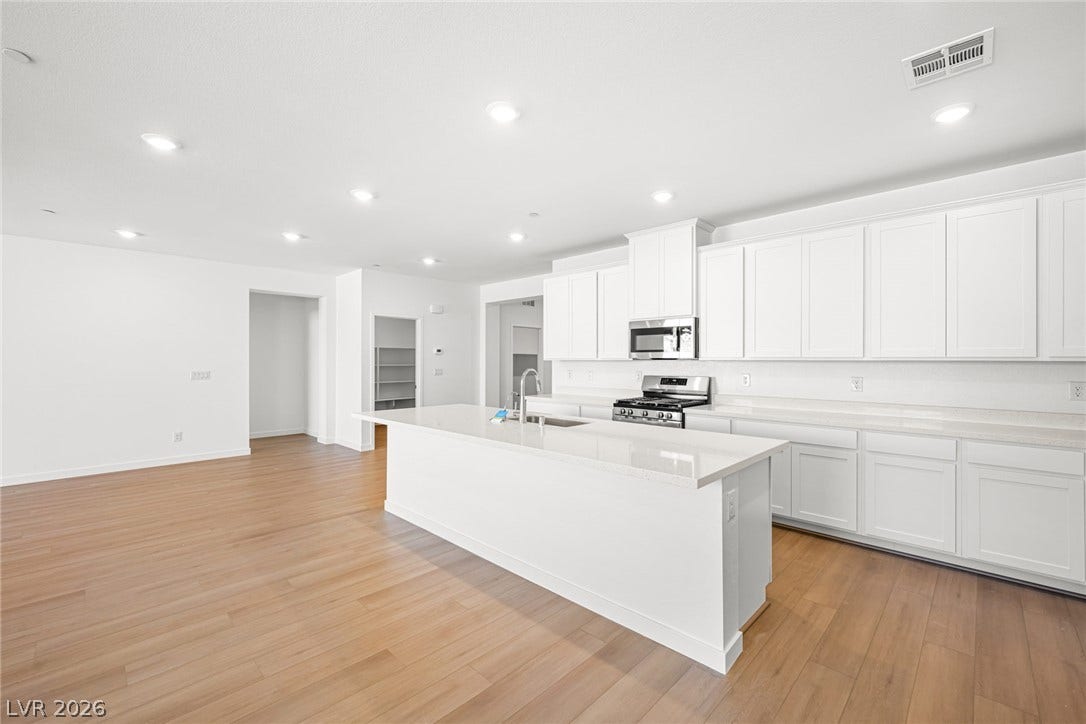 A well-lit kitchen featuring a spacious island, white cabinetry, and durable hardwood flooring.