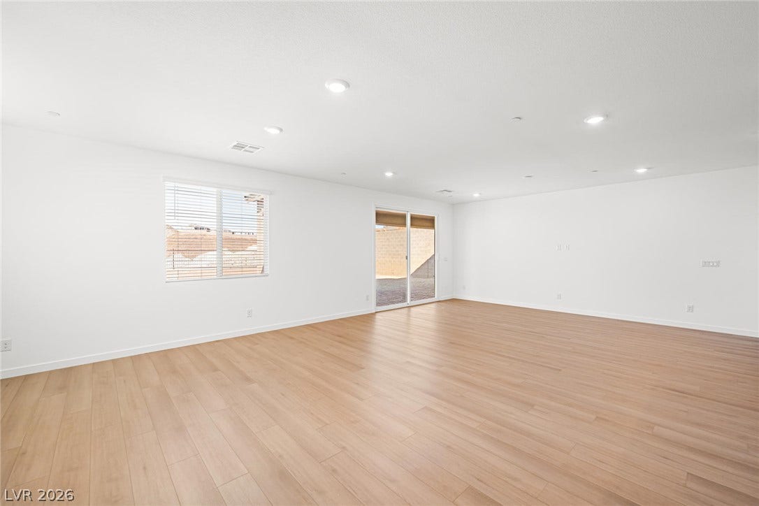 Recessed lighting illuminates this versatile space, featuring sleek hardwood flooring and a sliding glass door leading to the exterior.