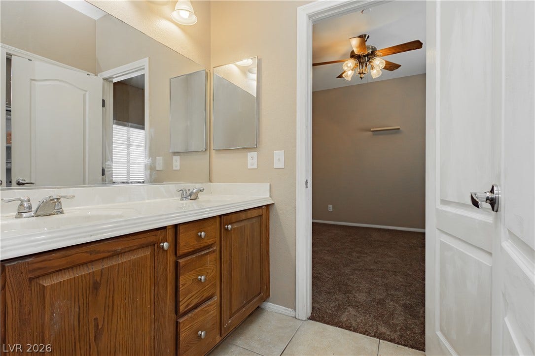1176 Via Piazza, Henderson, NV 89052 Double vanity with ample storage and an inviting view into a bedroom with a ceiling fan.