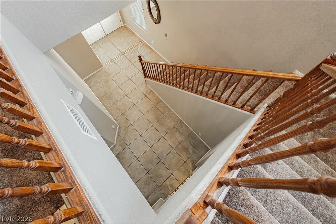 1176 Via Piazza, Henderson, NV 89052 A grand staircase with rich wooden banisters overlooks a tiled entryway, inviting exploration.