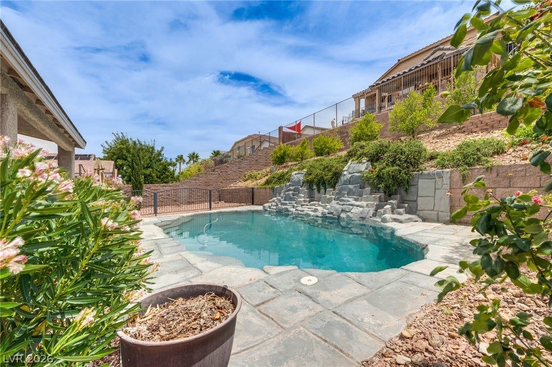 2393 Stansbury Court, Henderson, NV 89052 An inviting backyard oasis features a glistening pool with a rock waterfall feature and surrounding lush landscaping.