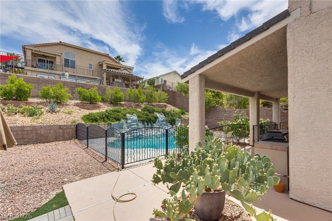 2393 Stansbury Court, Henderson, NV 89052 A tranquil backyard oasis features a fenced pool with a rock waterfall and covered patio.