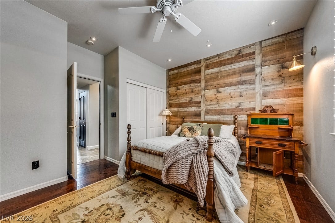 2393 Stansbury Court, Henderson, NV 89052 A comforting bedroom features a distinct reclaimed wood accent wall, hardwood floors, and a well-lit ceiling fan.