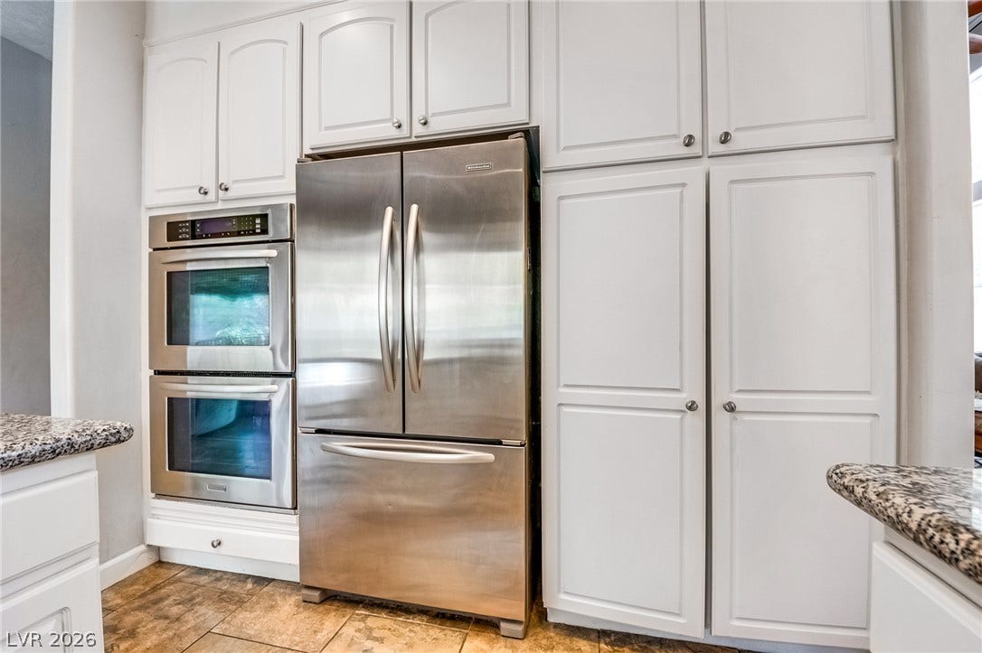 2393 Stansbury Court, Henderson, NV 89052 A contemporary kitchen features stainless steel appliances integrated seamlessly with crisp white cabinetry and granite countertops.