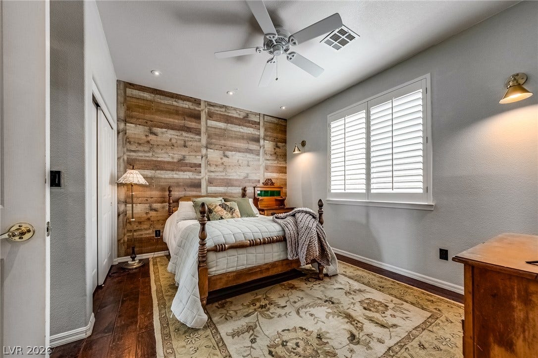2393 Stansbury Court, Henderson, NV 89052 A well-lit bedroom features hardwood flooring complemented by a decorative rug, and a rustic wood paneled accent wall.