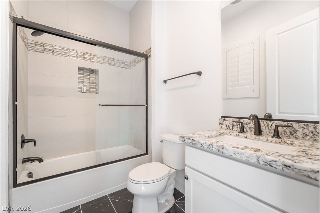 330 Meadow Brush Place, Henderson, NV 89011 A well-appointed bathroom features a glass-enclosed tub-shower combination, a toilet, and a vanity with a granite countertop.