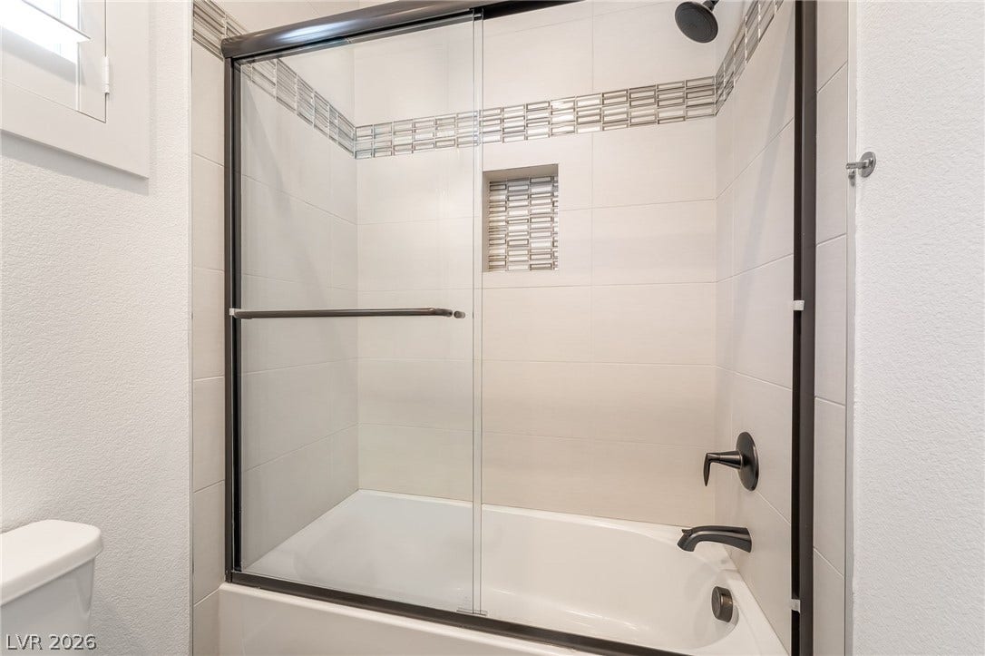 330 Meadow Brush Place, Henderson, NV 89011 A pristine bathroom features a shower-tub combination with sleek glass doors and stylish tiled accents.