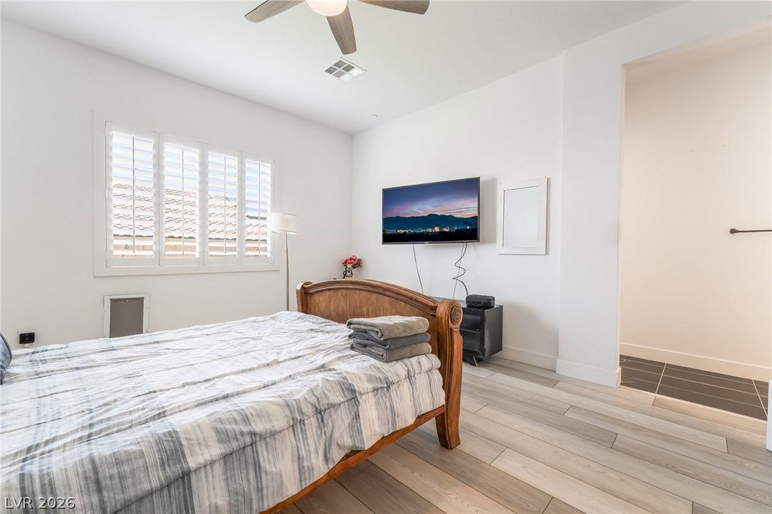 330 Meadow Brush Place, Henderson, NV 89011 A well-lit bedroom features cool-toned wood plank flooring and a modern ceiling fan for comfort.