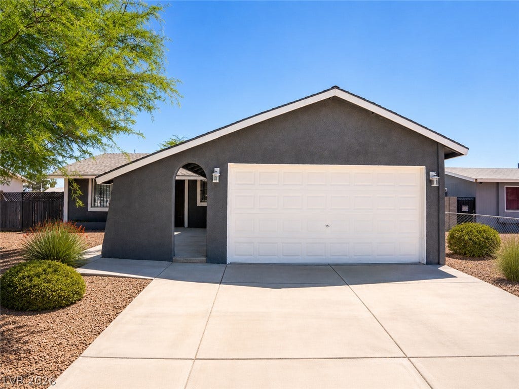 A dark gray stucco home with a bright white garage door, framed by a concrete driveway and simple landscaping.