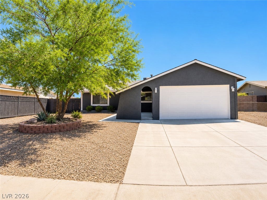 A dark-toned dwelling featuring a prominent white garage and xeriscaped front yard with a large shade tree.