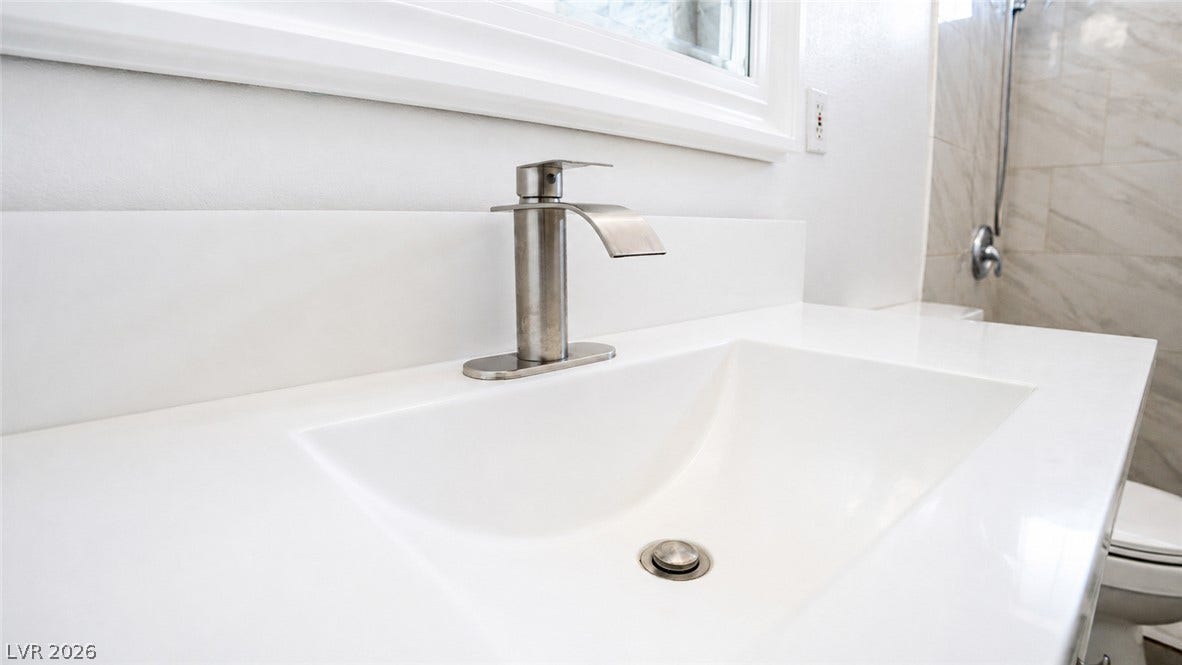 A sleek white vanity offers a pristine basin and modern faucet, complementing the bright bathroom.