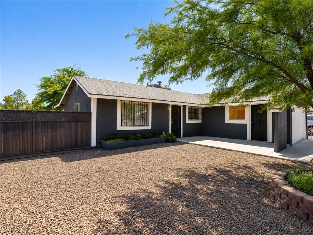 A well-maintained facade features secure windows, a wooden fence, and a gravel driveway.