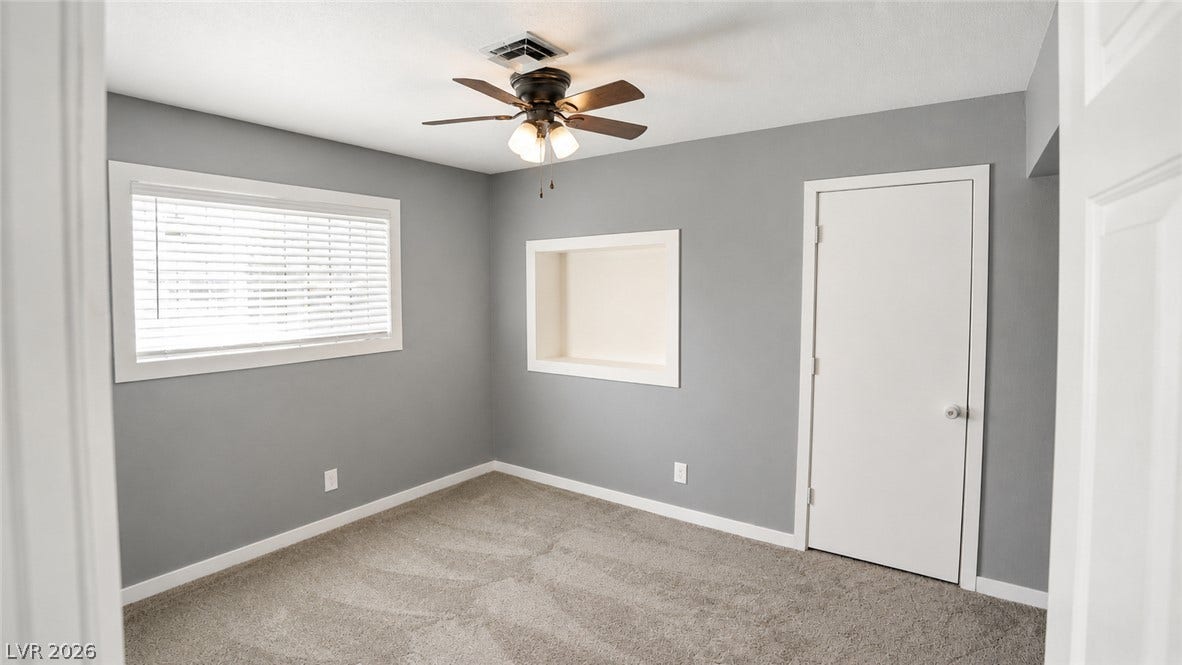A well-lit bedroom with plush carpet and a ceiling fan offers comfortable living.