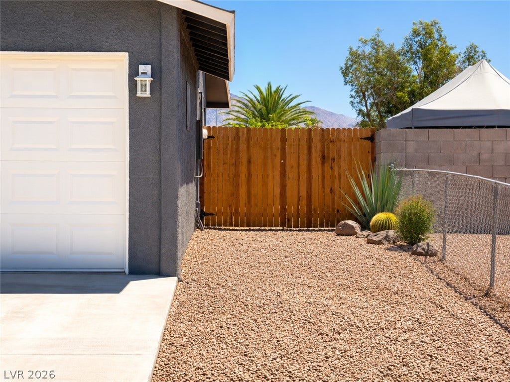A well-maintained side yard features a gravel ground, wood fence, and diverse desert plantings.