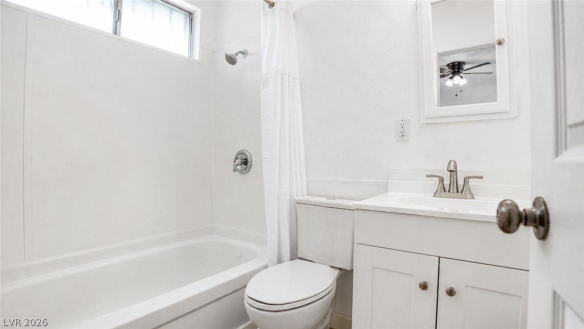 A pristine bath features a window above the shower, a well-appointed vanity, and a clean commode.