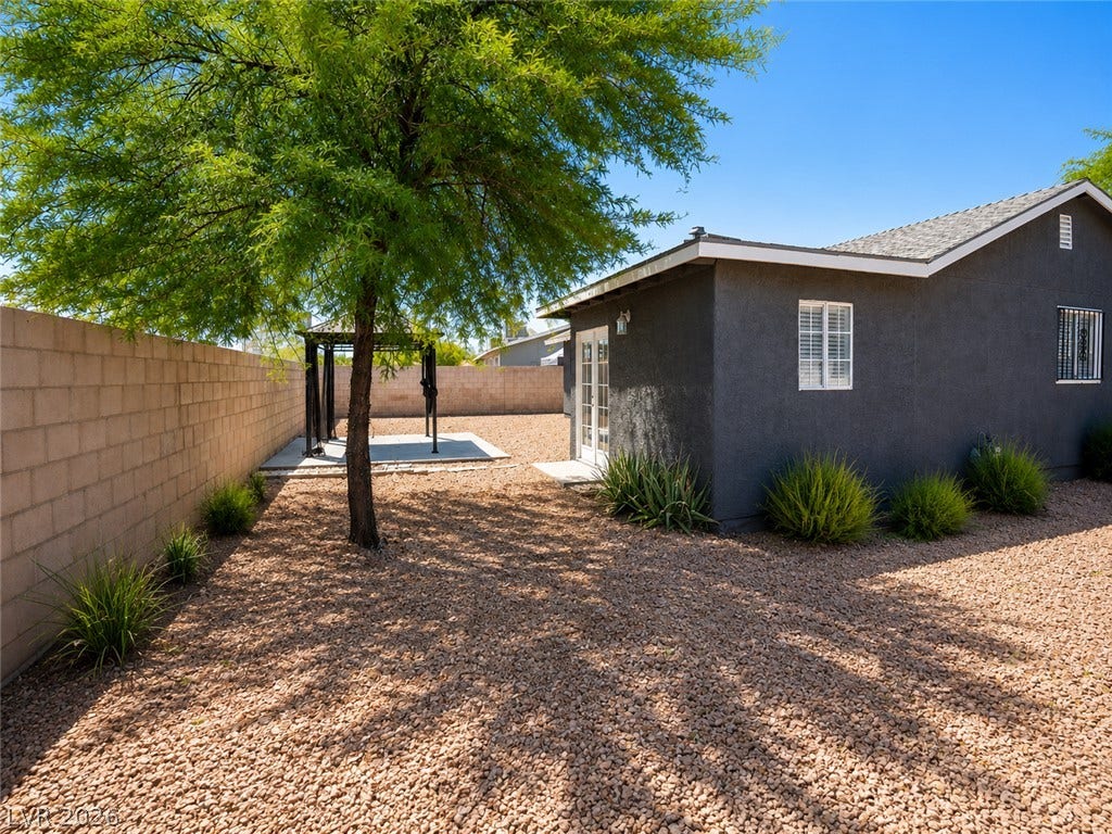 A well-maintained side yard features a sturdy block wall, gravel landscaping, and mature foliage providing pleasant shade.