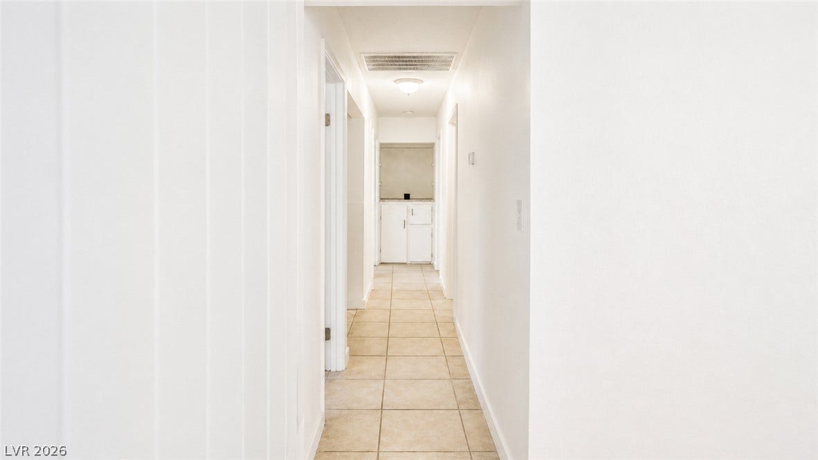 A well-lit corridor featuring tiled flooring, leading to a convenient built-in cabinet space.
