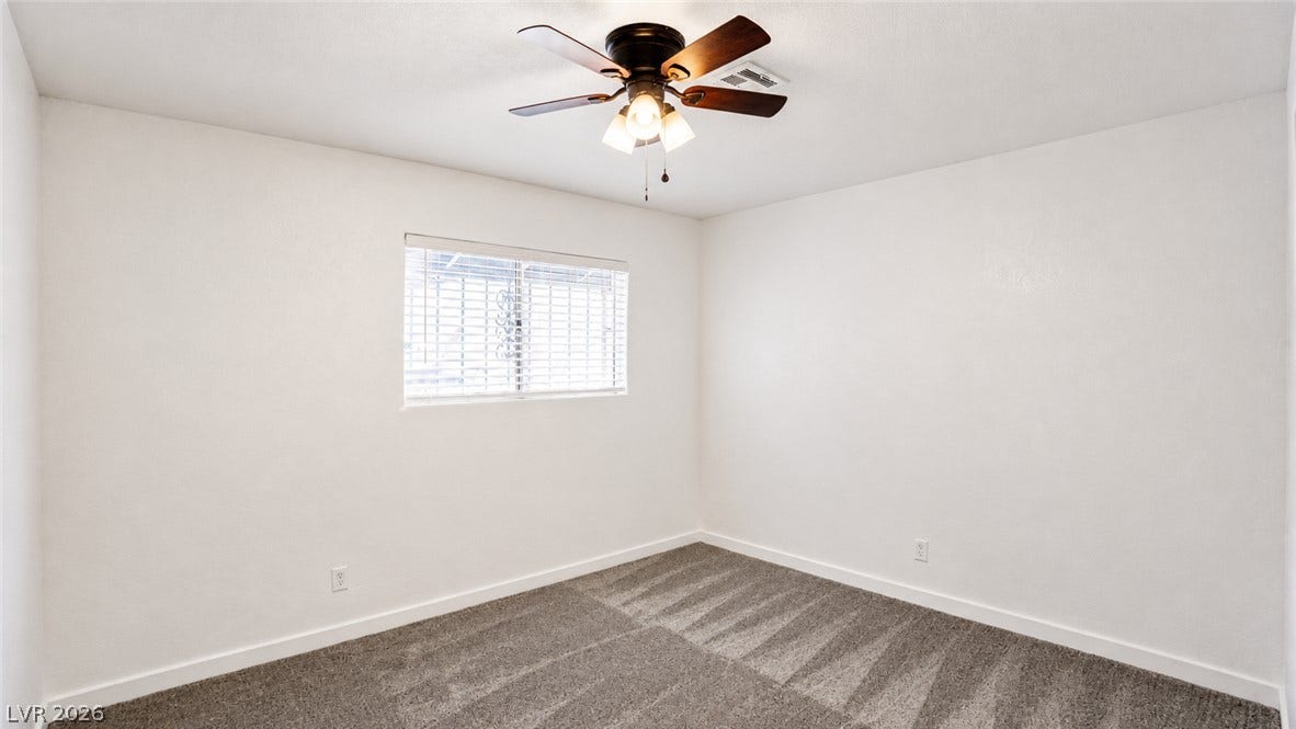 A versatile room with ample space features a ceiling fan and a window for natural light.