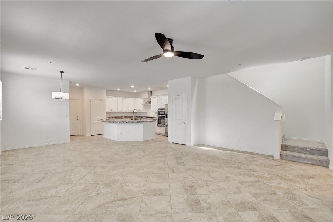 An open-concept living area with a ceiling fan, connecting to a contemporary kitchen with an island and integrated appliances.