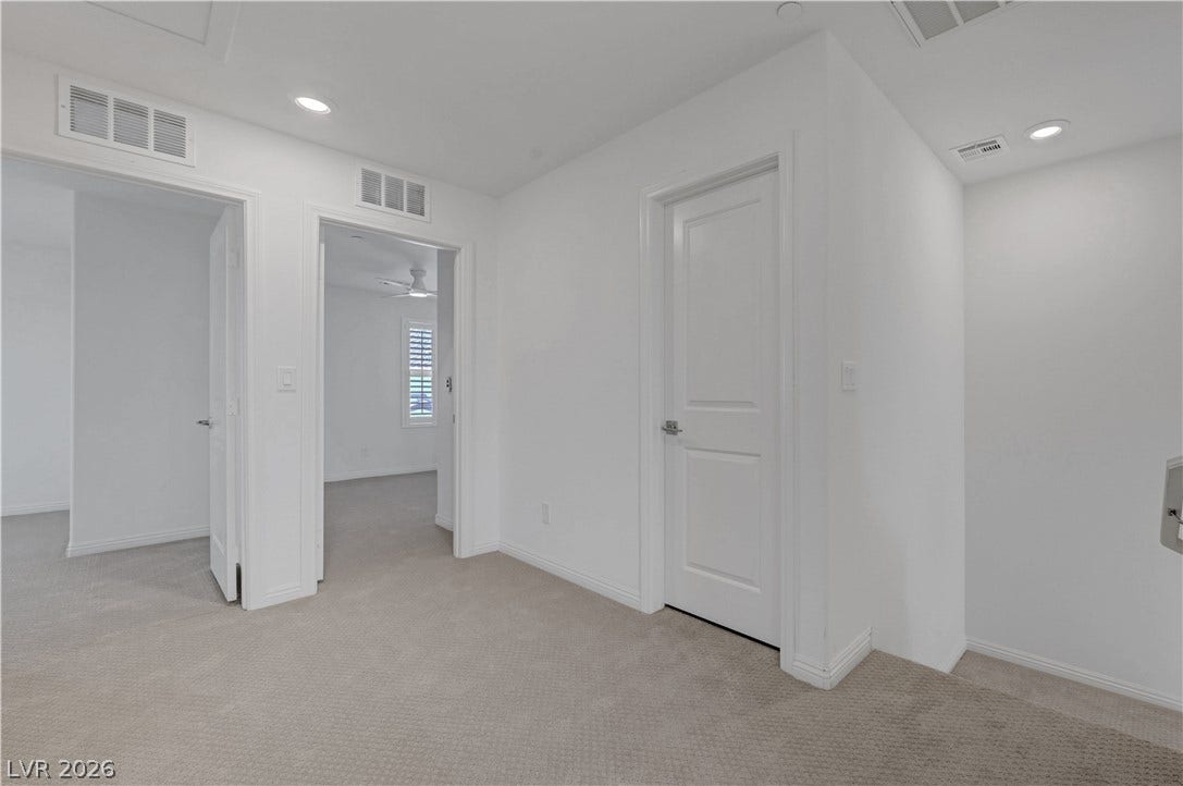 A well-maintained hallway with neutral carpet flooring and classic white walls, leading to additional rooms.