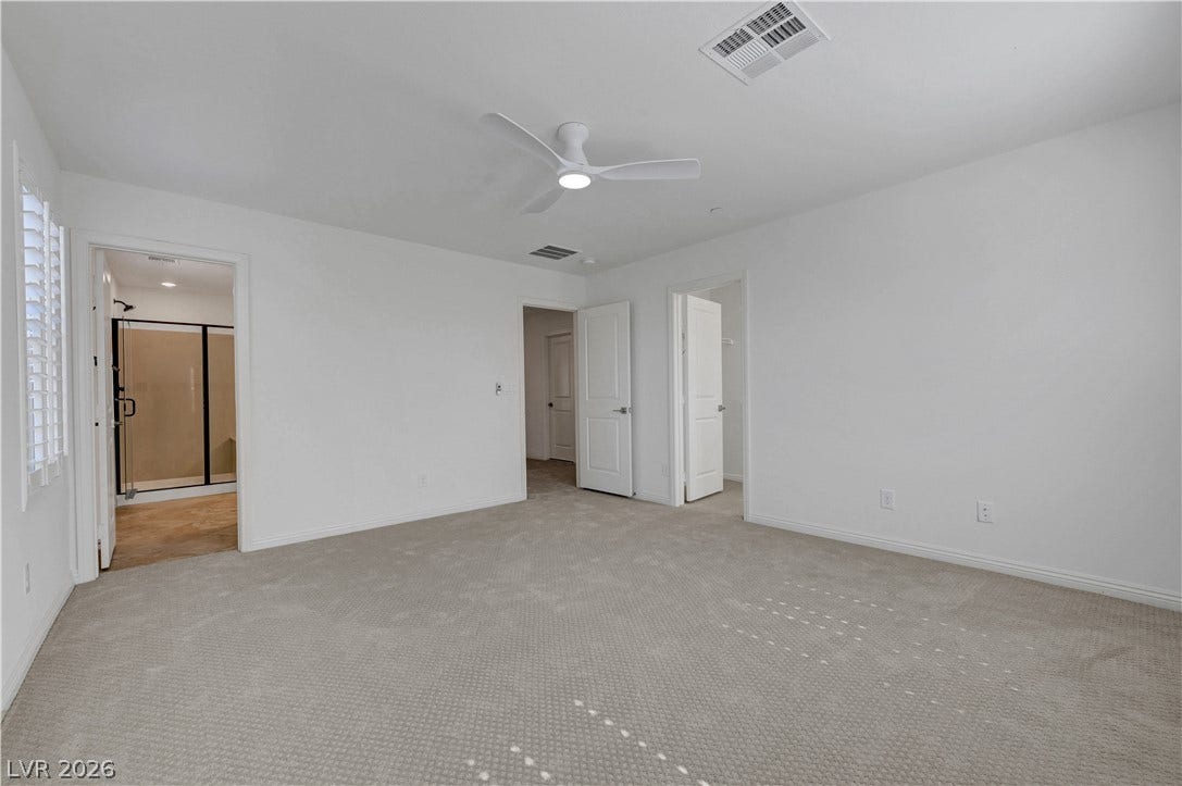 A spacious bedroom offers a modern ceiling fan and plush carpet, with an adjacent primary bathroom featuring a glass-enclosed shower.