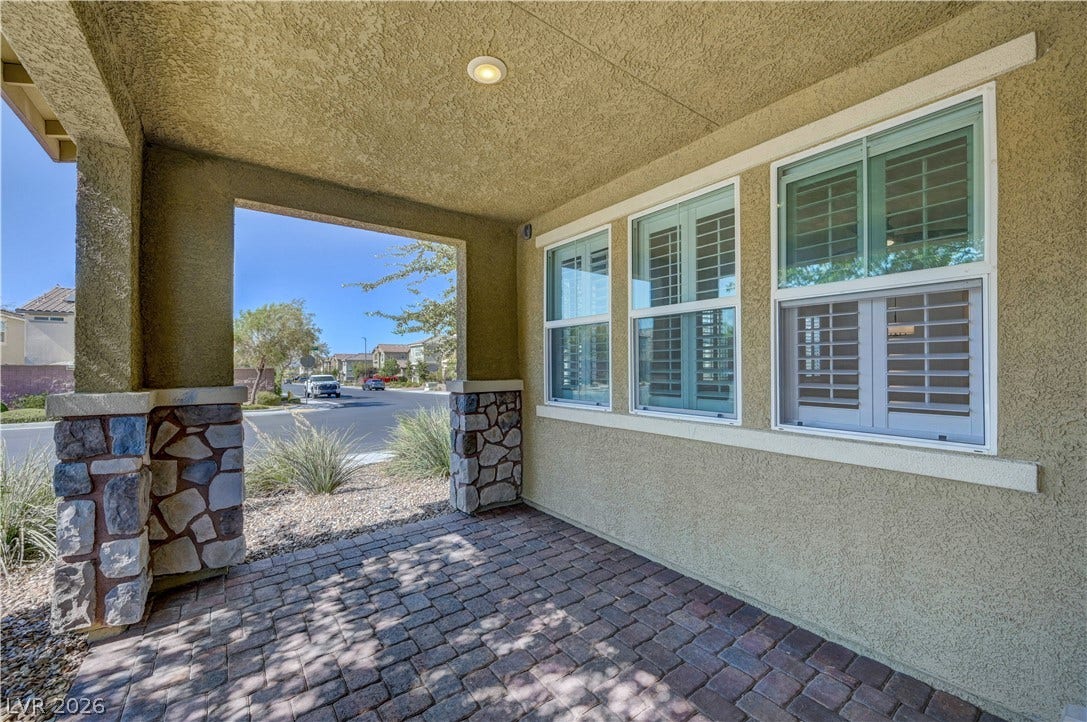 Enter through a welcoming front porch with decorative stone columns and a patterned paver floor.