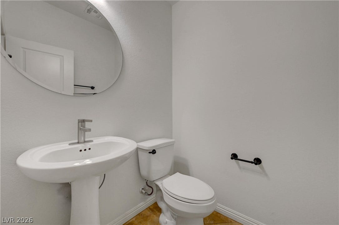 A well-appointed half bath features a sleek pedestal sink and complementary flooring.