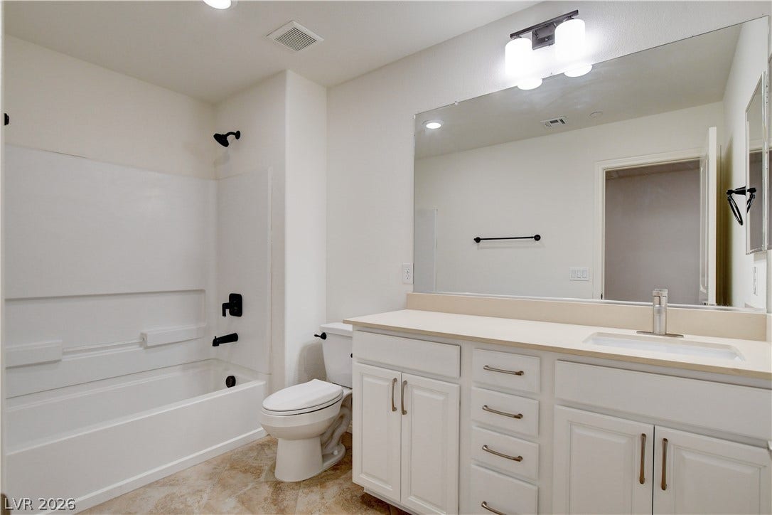 A well-lit bathroom features a functional tub-shower combination, modern vanity, and spacious mirror.