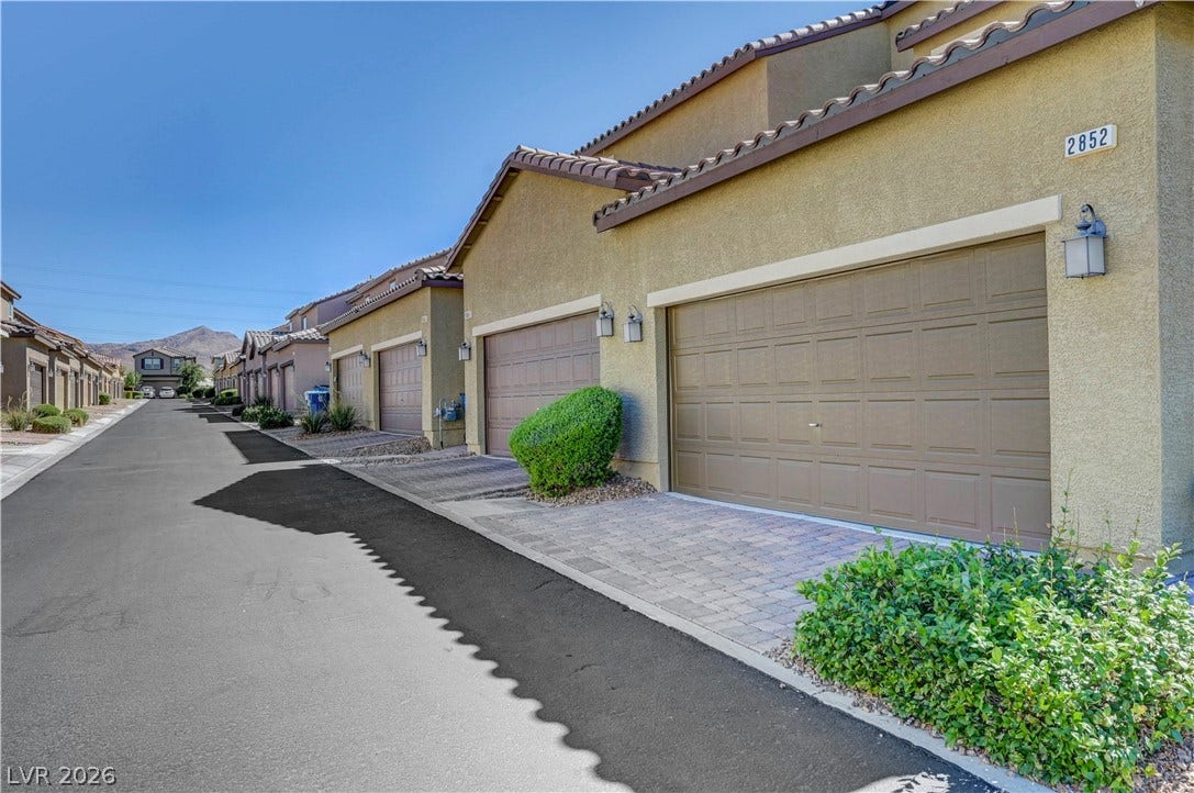 A row of garages line a paved road, featuring stucco exteriors and landscaped shrubbery.