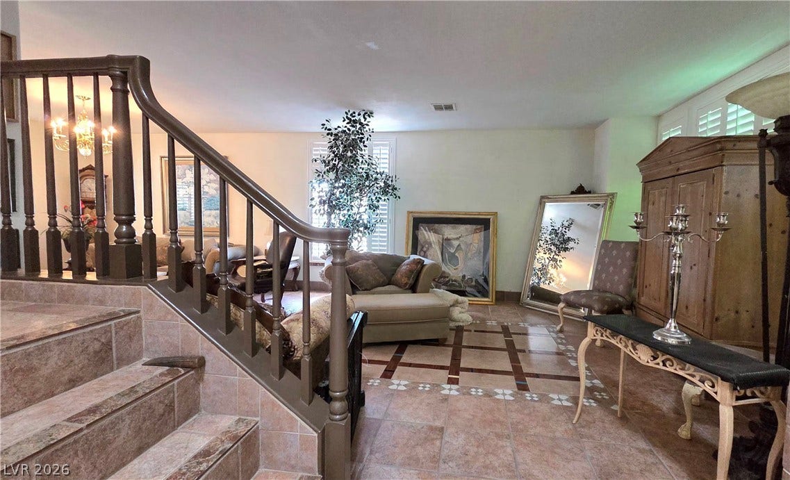 884 E Robindale Road, Las Vegas, NV 89123 A grand staircase with intricate wooden balusters leads to an elegant living area featuring patterned tile flooring.
