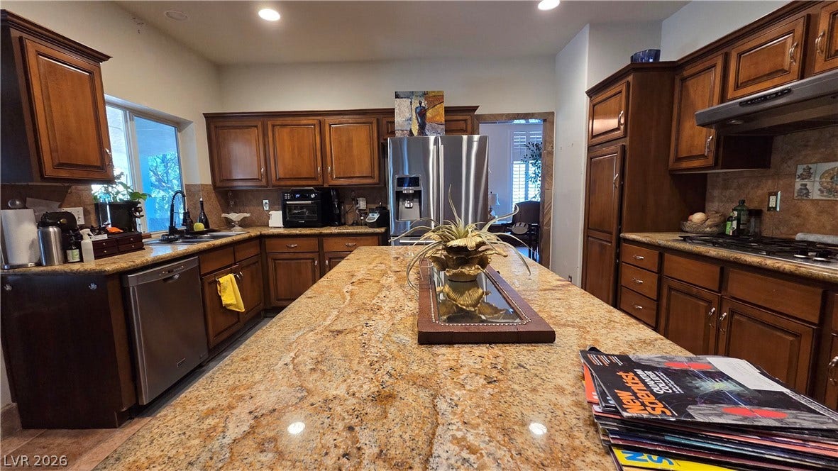 884 E Robindale Road, Las Vegas, NV 89123 A well-appointed kitchen features rich wooden cabinetry and a spacious granite-topped island, perfect for culinary endeavors.