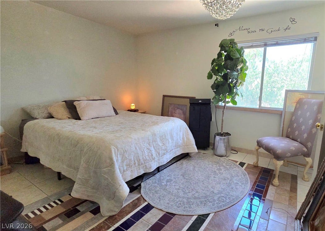 884 E Robindale Road, Las Vegas, NV 89123 An inviting bedroom with a crystal chandelier and patterned tile flooring, offering serene outdoor views.