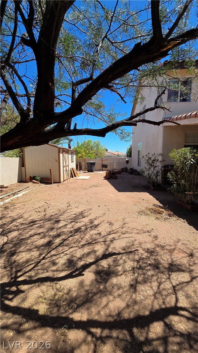884 E Robindale Road, Las Vegas, NV 89123 A spacious backyard with mature trees providing shade, featuring a practical storage shed.