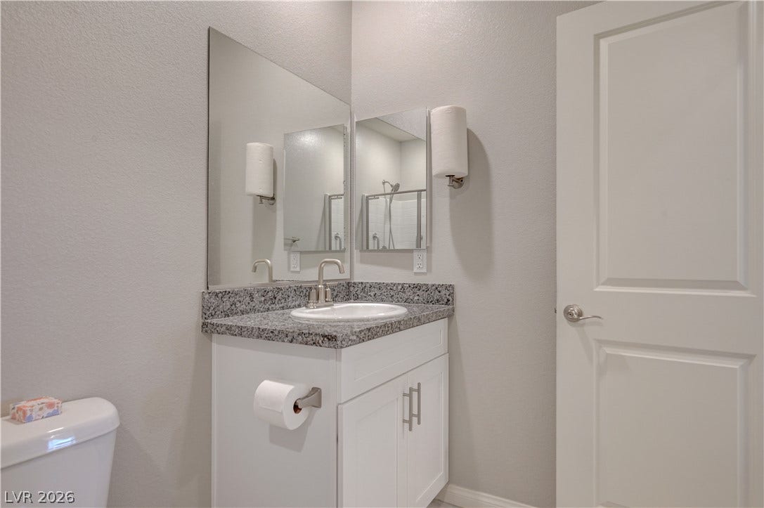 A well-appointed downstairs bathroom vanity features a sink with granite counters and ample cabinet storage, shower & tile floors.