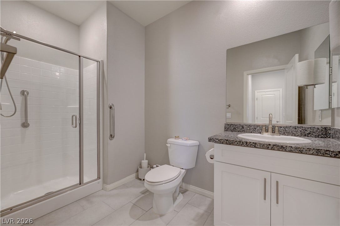 A well-appointed downstairs bathroom vanity features a sink with granite counters and ample cabinet storage, shower & tile floors.