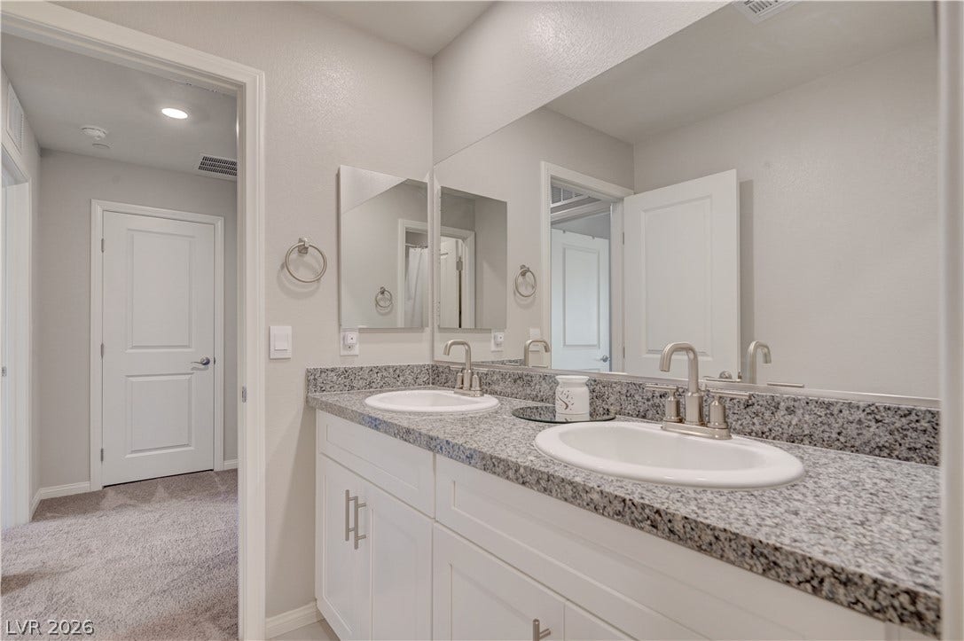 Double vanity with granite counters and expansive mirrors elevate this practical bathroom space.