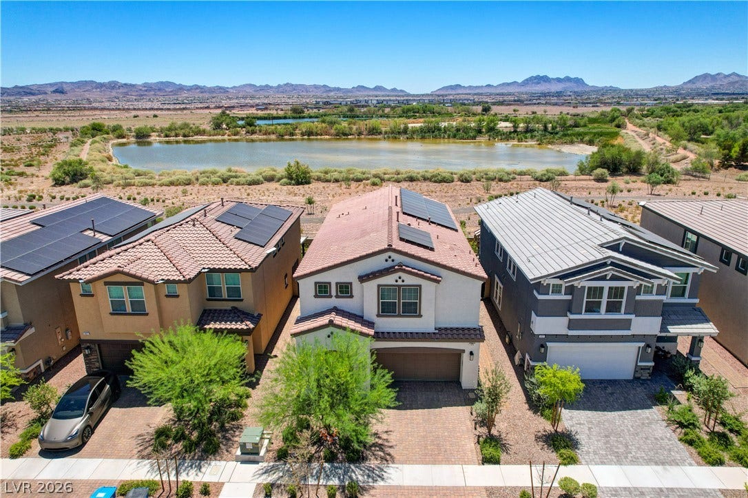 A desert-modern residence with a tile roof, solar panels, and a paver driveway, offering scenic views of a tranquil lake and distant mountains.