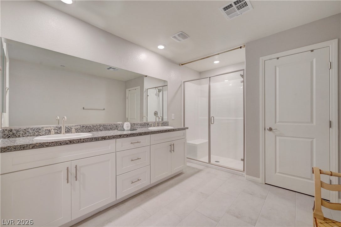 Dual vanities with granite counters and a spacious glass-enclosed shower create a practical primary bath.